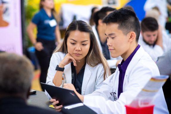 Students in white coats looking at laptop.